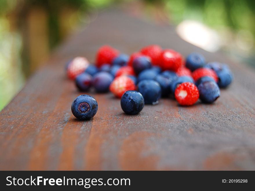 Delicious forest bilberries and wild strawberries. Close-up on the wooden background, shallow dof. Delicious forest bilberries and wild strawberries. Close-up on the wooden background, shallow dof