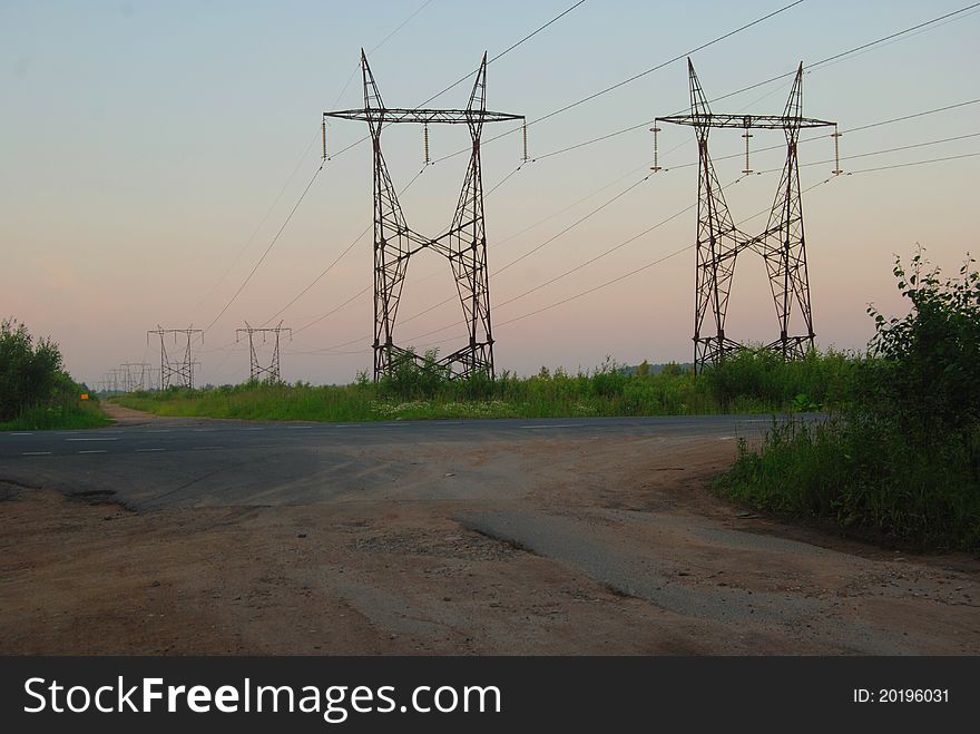 Landscape with high-voltage line over the asphalted road. Warm evening light and clear sky