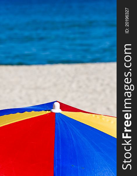 Colorful beach umbrella with white beach and blue sea background