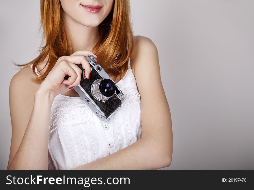 Redhead girl in white dress with vintage camera. Studio shot.
