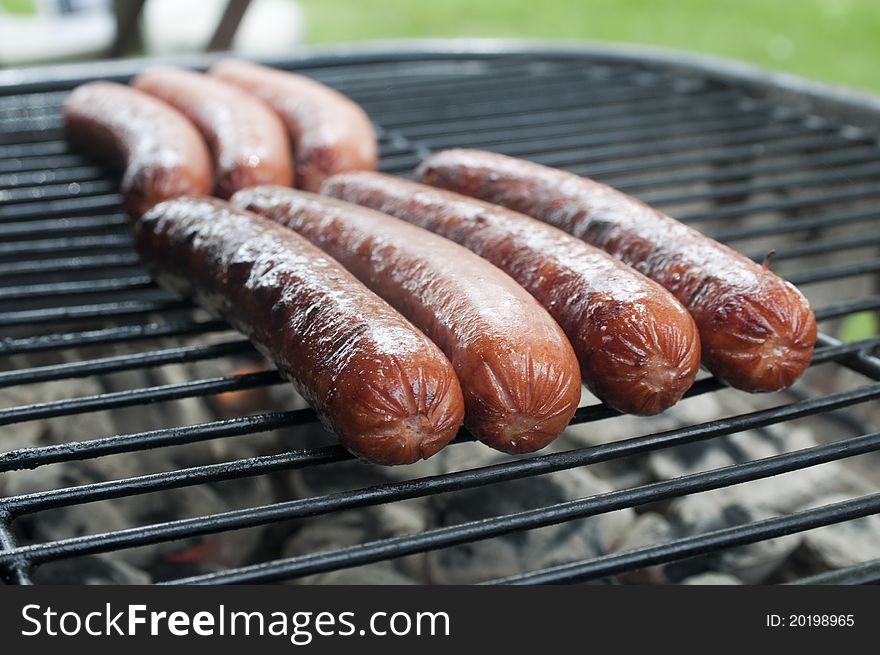 Hot dogs cooking on the grill. Macro focus on the end of the foreground row of hot dogs. Hot dogs cooking on the grill. Macro focus on the end of the foreground row of hot dogs.