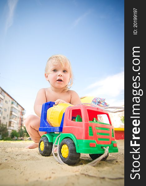 Adorable baby play with toy concrete mixer truck on playground on sand