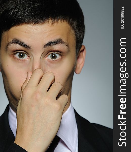 Expressions Young handsome business man touching his nose . studio shot