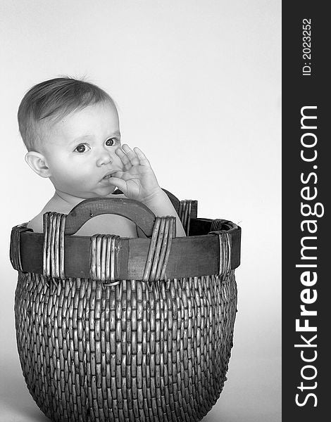 Black and white image of cute baby sitting in a woven basket. Black and white image of cute baby sitting in a woven basket