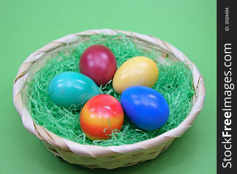 Five colored eggs in basket on green background
