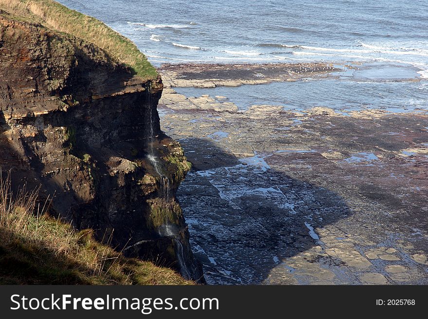 View of a waterfall tumbling down a coastal cliff. View of a waterfall tumbling down a coastal cliff.