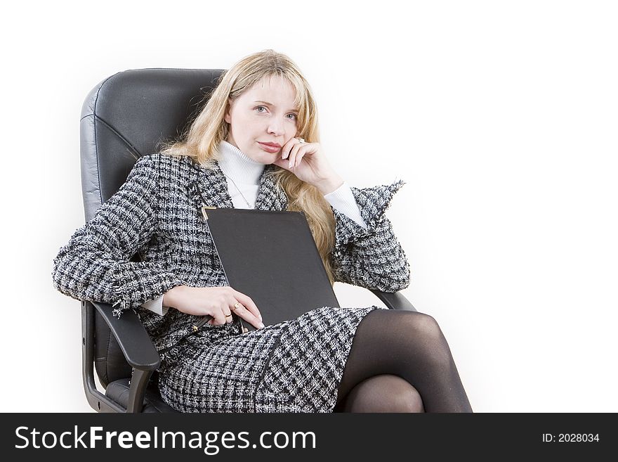 A woman wearing a suit and holding a folder sitting in a black chair. A woman wearing a suit and holding a folder sitting in a black chair