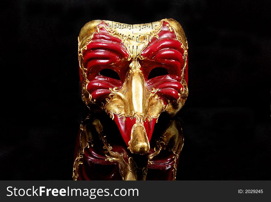 Traditional Venetian Mask in red and gold against reflective black background