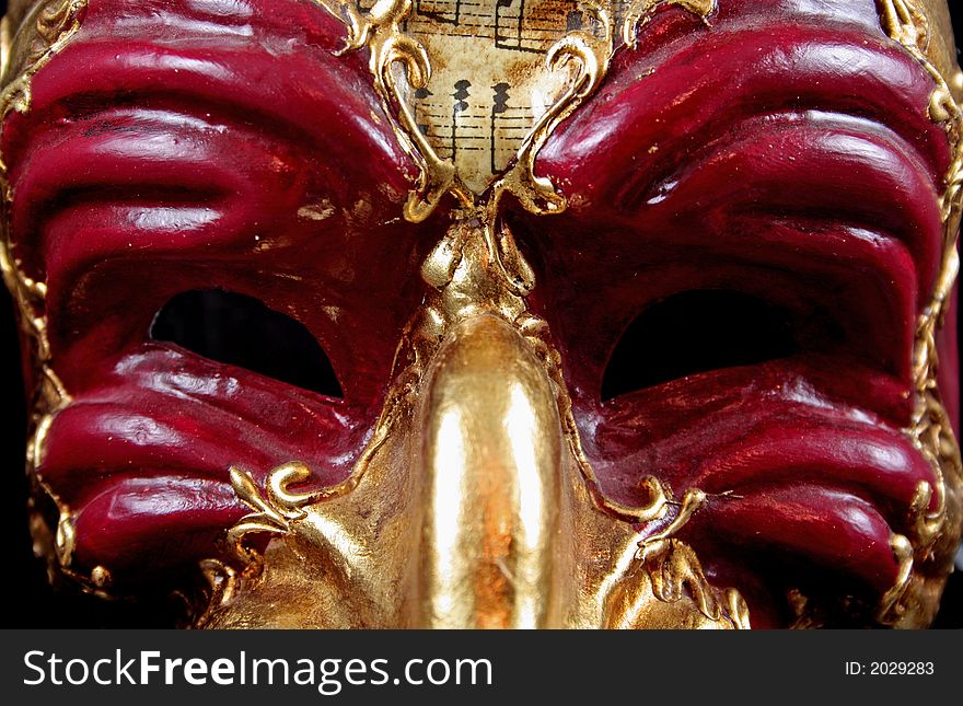 Traditional Venetian Mask in red and gold against reflective black background