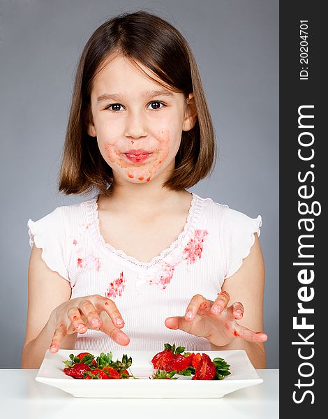 Portrait of cute little girl eating strawberries in the studio, grey background