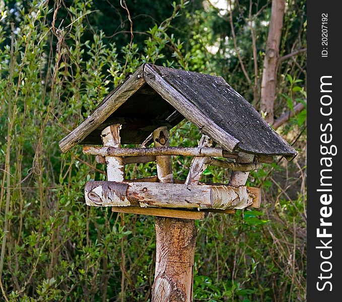 Bird feeder was made from wood. bushes are in the background. Bird feeder was made from wood. bushes are in the background