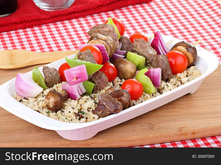 Beef kabobs with onion, peppers, tomatoes,and mushrooms on top of rice