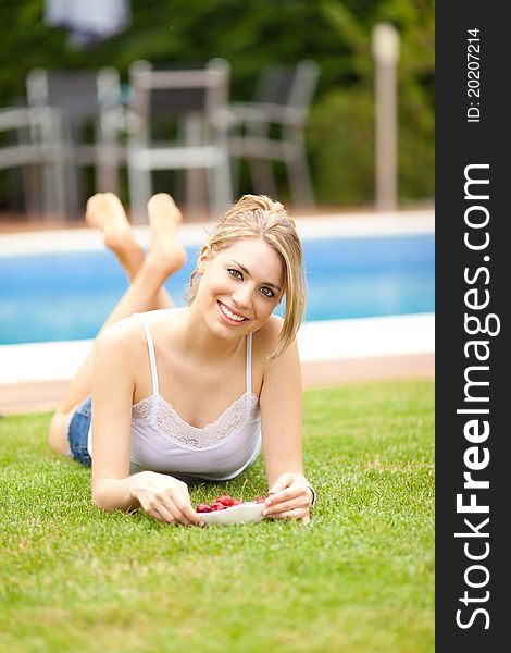 Young beautiful blonde woman eating cherries on the grass smiling. Young beautiful blonde woman eating cherries on the grass smiling