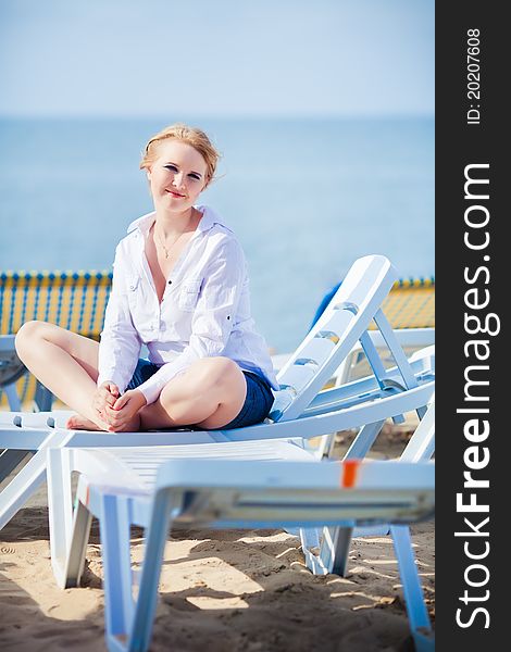 Beautiful woman sitting in chaise on the beach