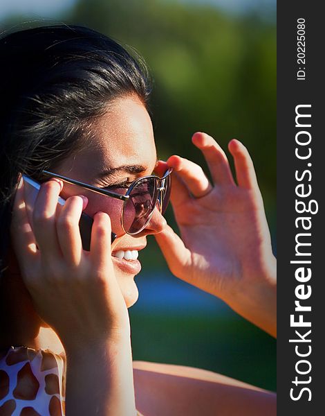 Portrait of a beautiful woman wearing sunglasses outdoors in the park talking on mobile phone. Portrait of a beautiful woman wearing sunglasses outdoors in the park talking on mobile phone