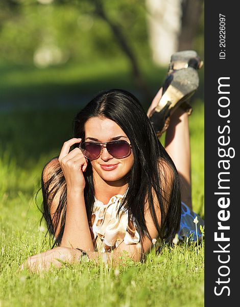 Beautiful brunette in sunglasses lying on the grass on a summer day. Beautiful brunette in sunglasses lying on the grass on a summer day