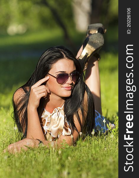 Beautiful brunette in sunglasses lying on the grass on a summer day. Beautiful brunette in sunglasses lying on the grass on a summer day