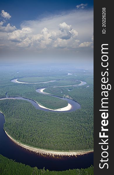 Aerial view of the river which doing loops in the woods under the white clouds. Aerial view of the river which doing loops in the woods under the white clouds.