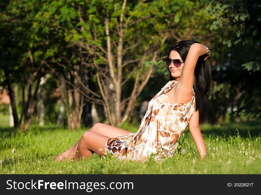 Beautiful brunette in sunglasses sitting on the grass on a summer day. Beautiful brunette in sunglasses sitting on the grass on a summer day