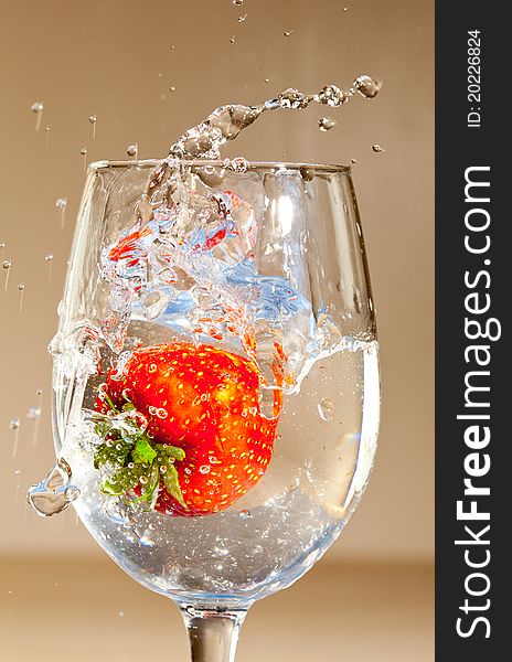 A single strawberry splashing in a glass of liquid.