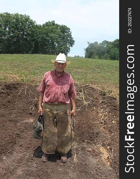 Farrier wearing chaps holding the tools of his trade in his hands.