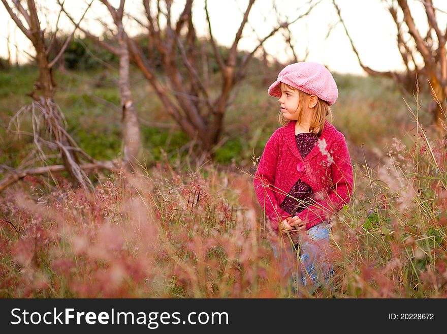 Young girl wearing a knit hat and sweater, standing in a field of tall grass and wildflowers. Horizontal shot. Young girl wearing a knit hat and sweater, standing in a field of tall grass and wildflowers. Horizontal shot.