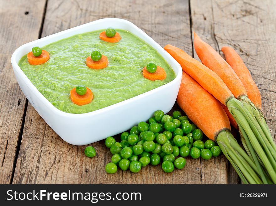 Fresh vegetable dish of green peas with carrots on wooden table