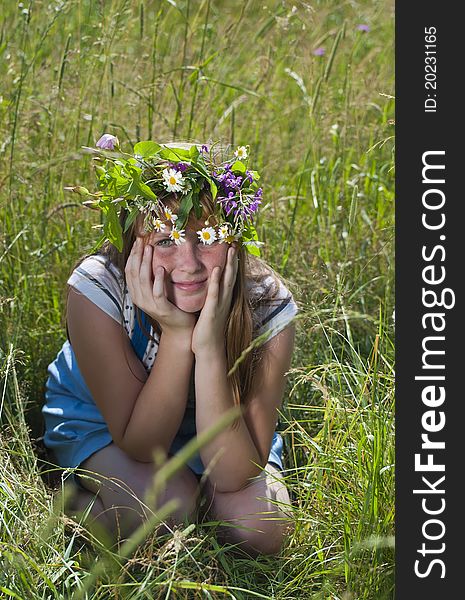 The red-haired girl with a wreath sits on the grass. The red-haired girl with a wreath sits on the grass