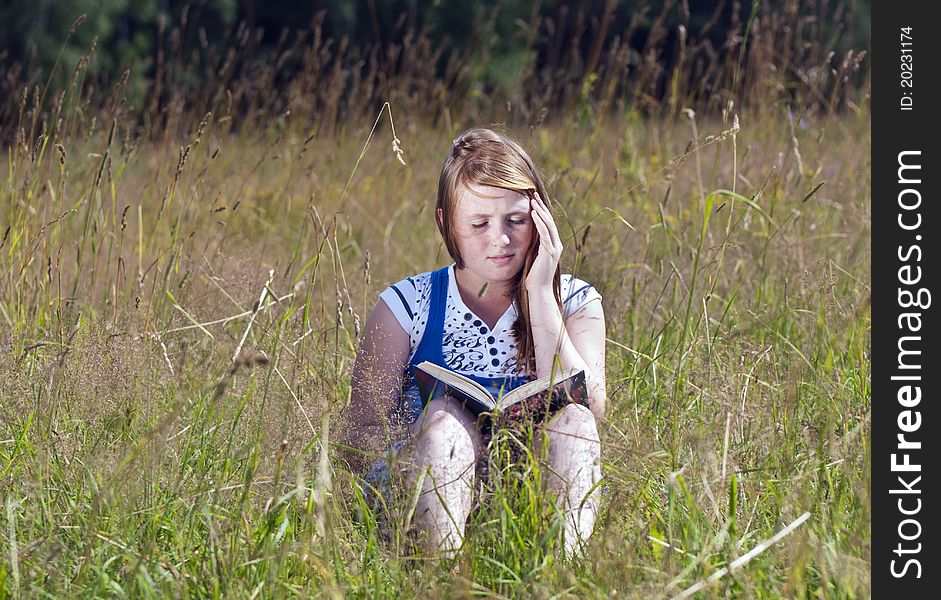 The red girl in the field reads the book. The red girl in the field reads the book
