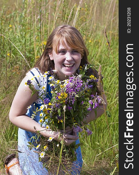 The happy red girl in the field with a bunch of flowers