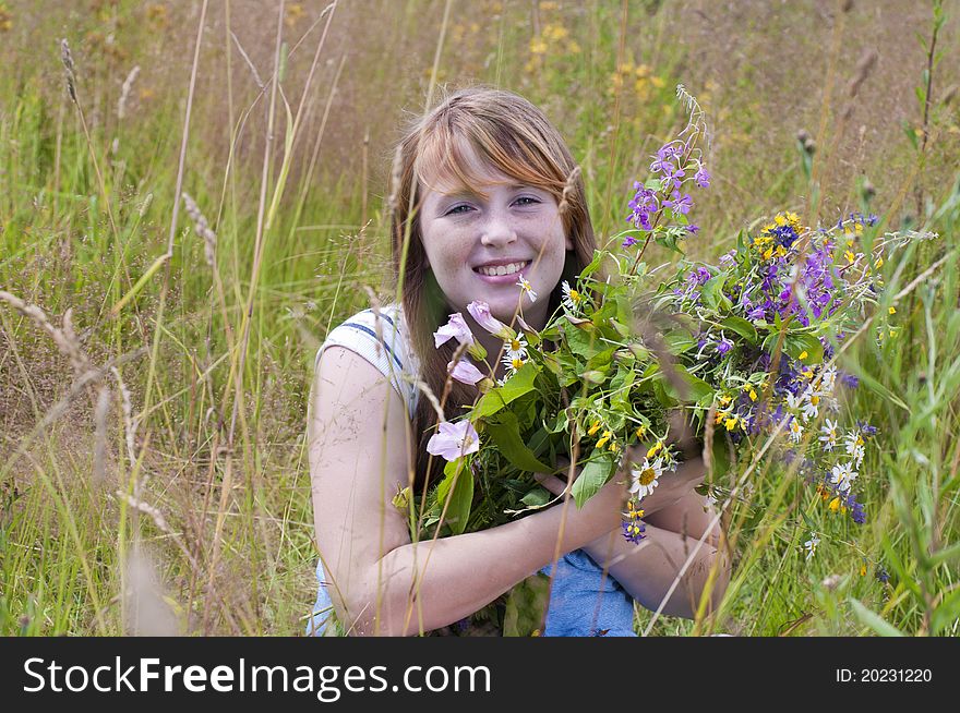 The smiling red girl in the field with a bouquet of flowers. The smiling red girl in the field with a bouquet of flowers