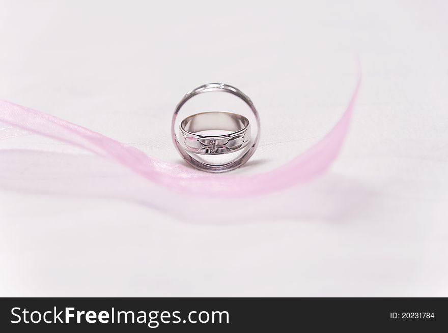 Silver wedding rings with pink ribbon on foreground