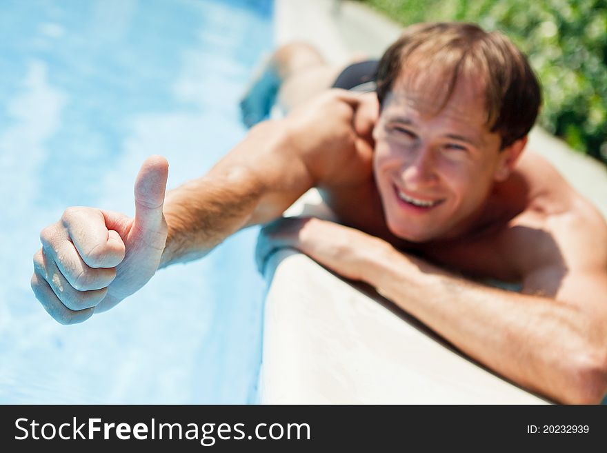 Young smiling man showing thumb up near the swimming pool. Young smiling man showing thumb up near the swimming pool