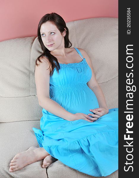 Pregnant woman in blue dress sitting on couch in living room. Pregnant woman in blue dress sitting on couch in living room