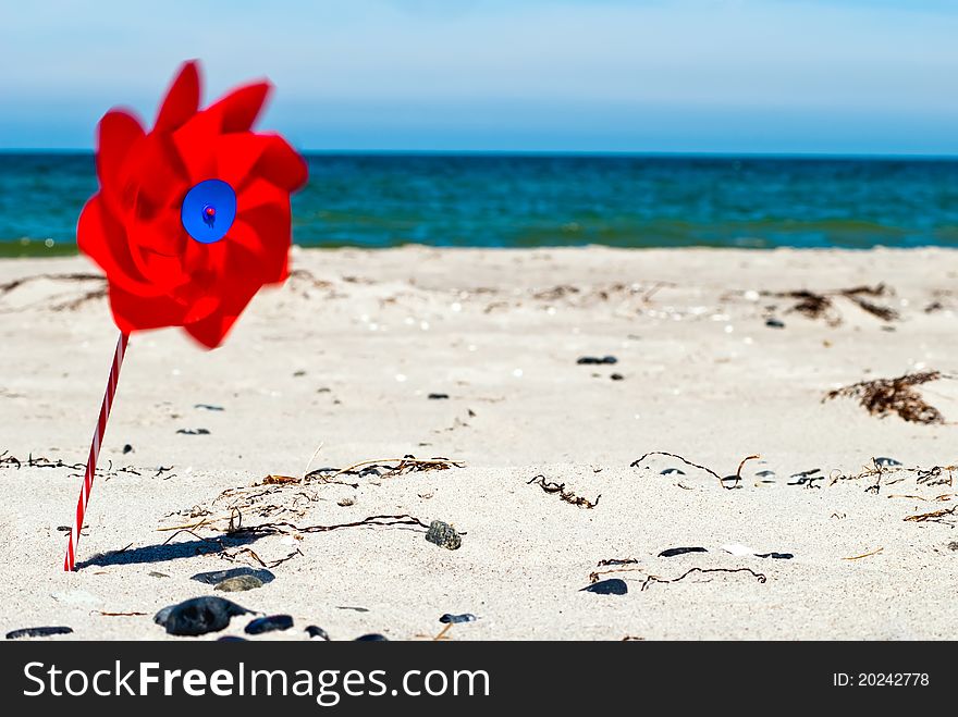 A red wind turbine on the sandy beach with sea in the background. A red wind turbine on the sandy beach with sea in the background