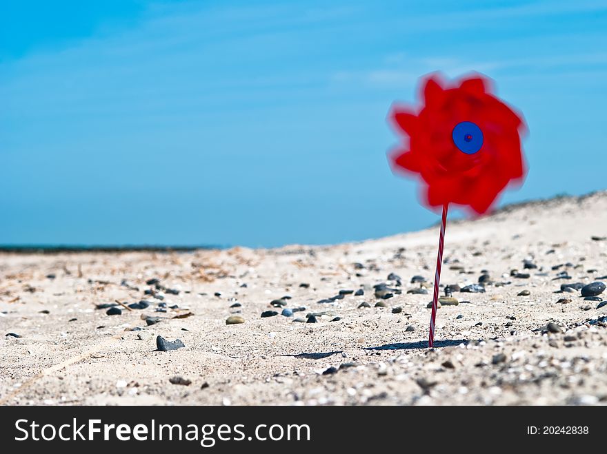 A red wind turbine on the sandy beach with sea in the background. A red wind turbine on the sandy beach with sea in the background