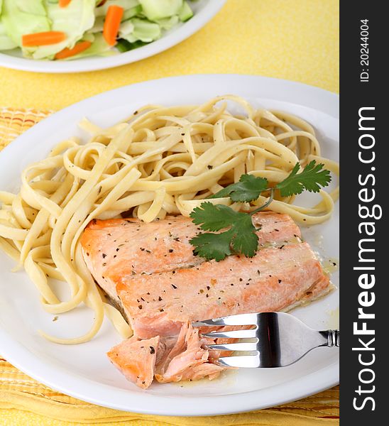 Salmon fish fillet cut with a fork with noodles on a plate