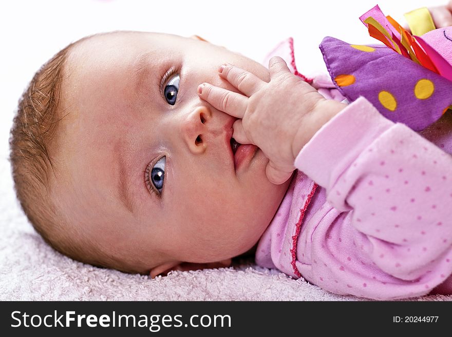 Newborn baby is sucking finger and playing with a colourful toy. Newborn baby is sucking finger and playing with a colourful toy