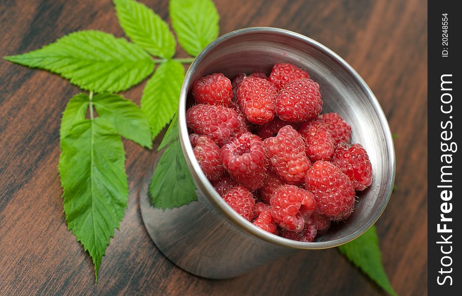 Pile of Raspberries in iron glass on wooden background