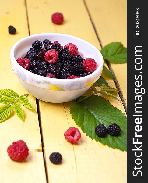 Blackberry and raspberry in white cup with green leaves. Blackberry and raspberry in white cup with green leaves