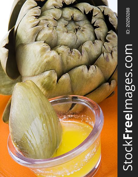 Steamed artichoke with melted butter on an orange ceramic plate