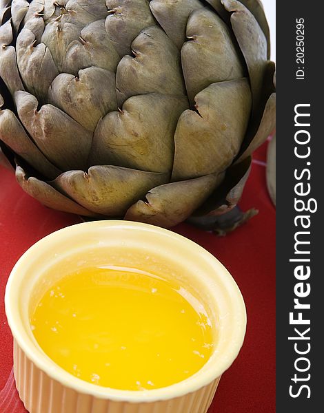 Steamed artichoke with melted butter on a red ceramic plate