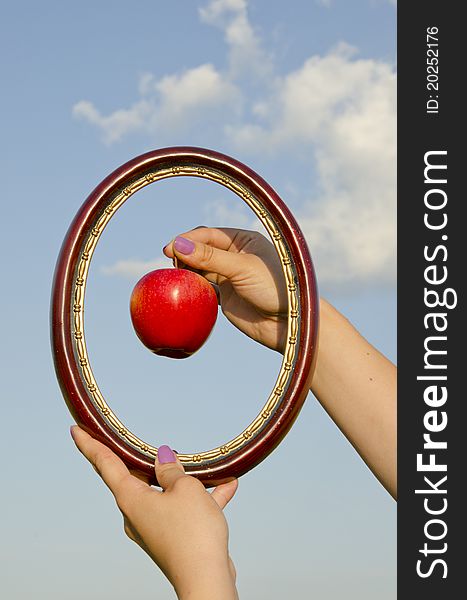 Woman hands with frame and apple on sky background