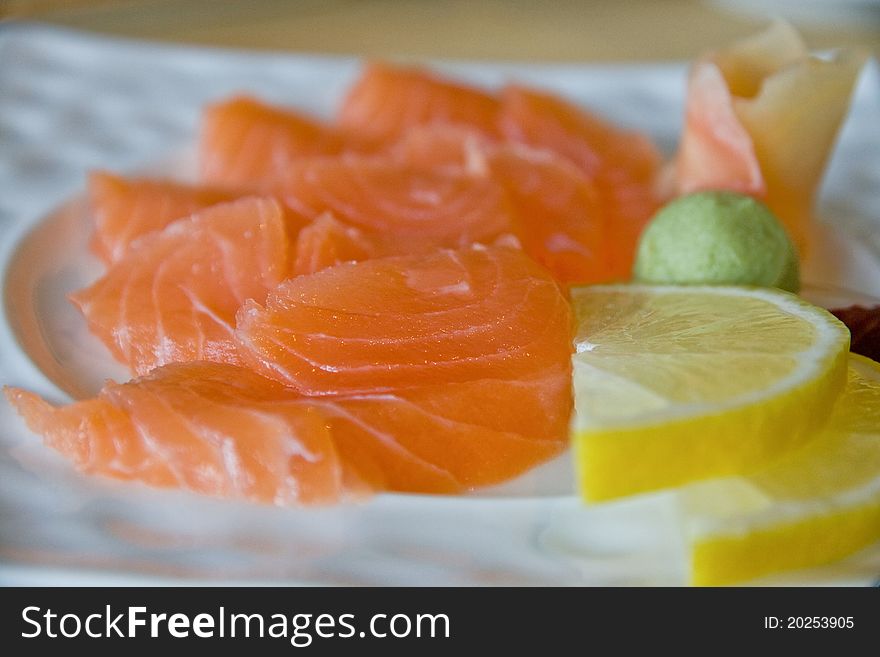 Salmon sashimi close-up with lemon, wasabi and ginger on a white plate