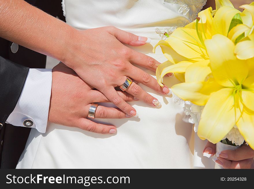 Bride and groom hands with wedding rings and bouquet