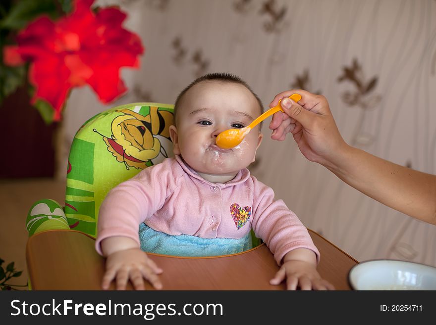 Ittle girl baby sitting for children's table and eat with a spoon feeds her mother. Ittle girl baby sitting for children's table and eat with a spoon feeds her mother