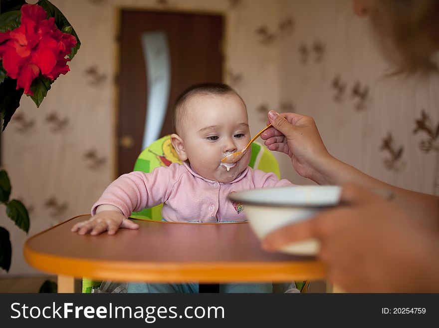 Ittle girl baby sitting for children's table and eat with a spoon feeds her mother. Ittle girl baby sitting for children's table and eat with a spoon feeds her mother