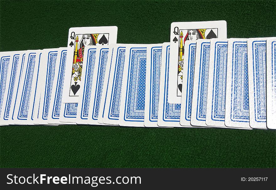 Deck of cards face-down on the green playing table with two Queens of Spades