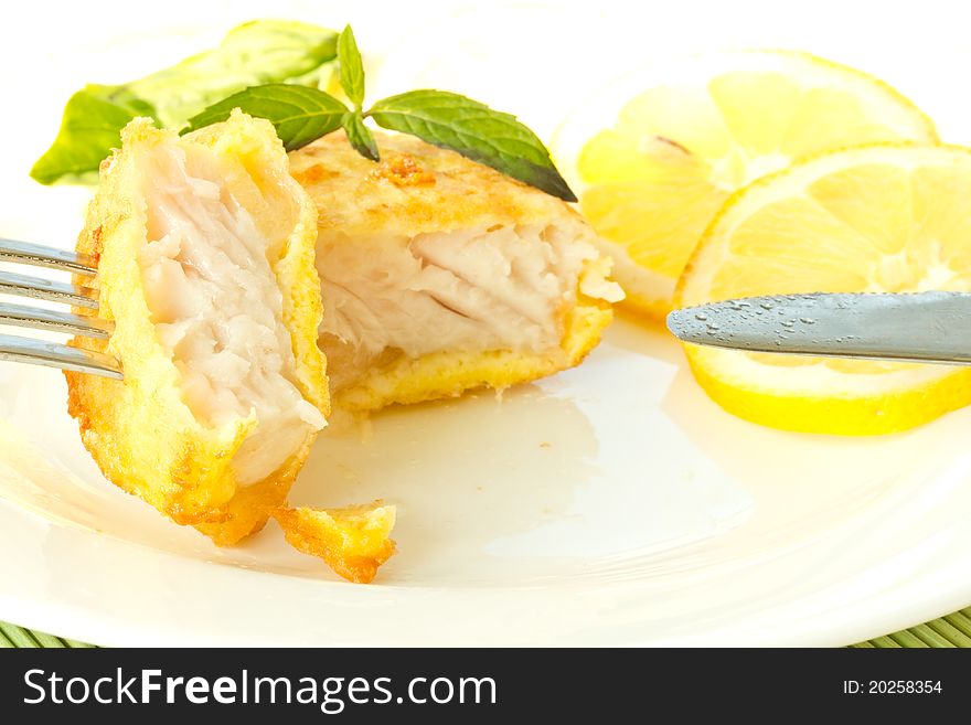 Fish fillets fried in batter with lemon and basil on a plate