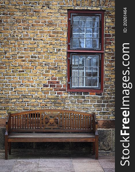 Empty bench below window, situated against an old brick wall.